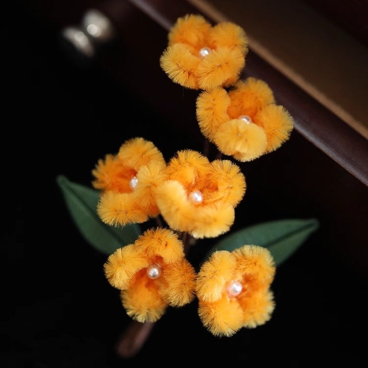 osmanthus-inspired floral brooch on a winter coat displayed on fabric