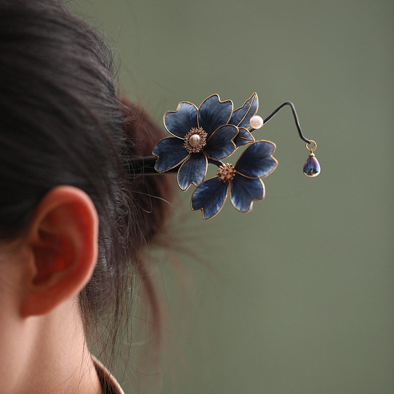 A navy blue floral hair accessory with pearl, leaf, and dangling details, secured beside a bun.