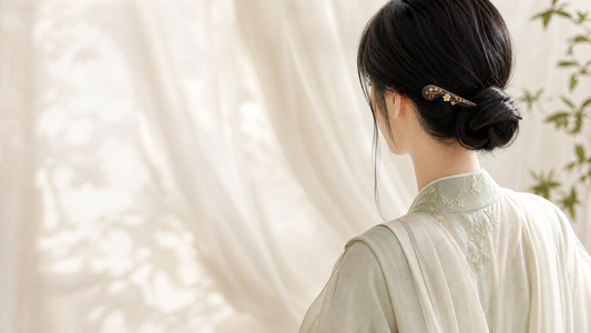 A woman in a Hanfu-inspired outfit wearing a dark floral hairpin in a low bun.
