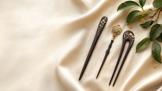 Three Chinese-inspired hair accessories—a single-prong hairpin, a hair stick, and a two-prong hair fork—arranged on ivory silk.