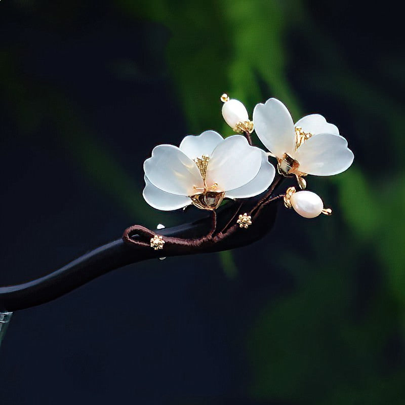 Warm bronze floral hair stick placed on dark fabric, showing carved flower detail and slender shaft