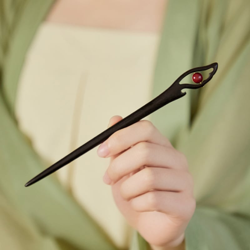 Red lacquered wood-look stick with carved floral motif tucked into bun