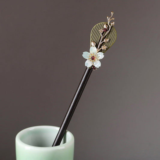 Dark wooden hair stick with carved floral motif set diagonally in bun.