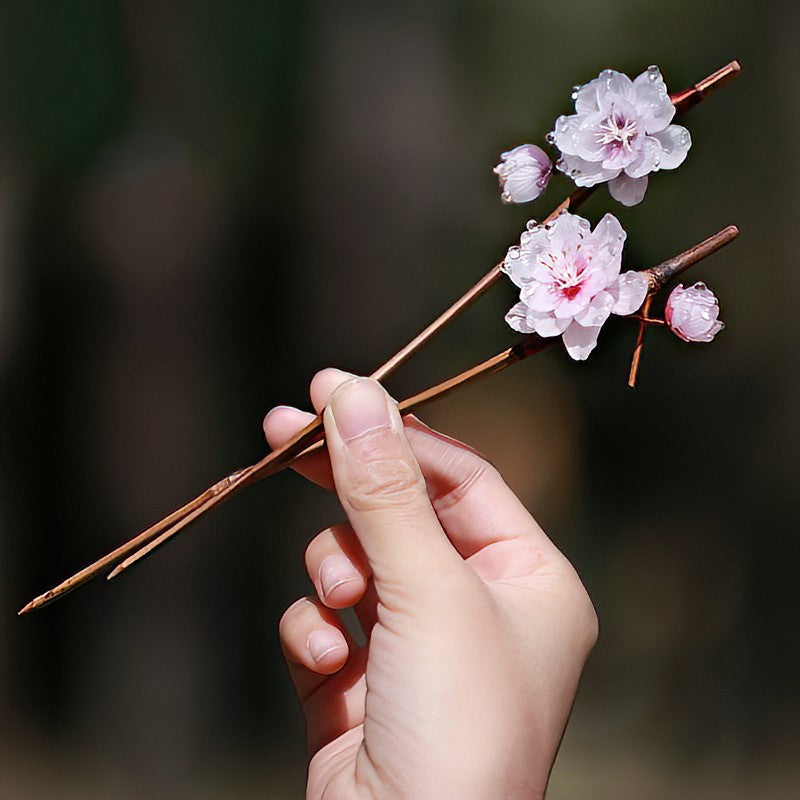 Pair of wood-look sticks crossing over a loose braided updo on neutral background
