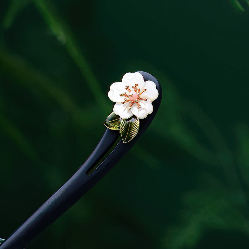 Dark polished hair stick with pale carved flower resting on linen
