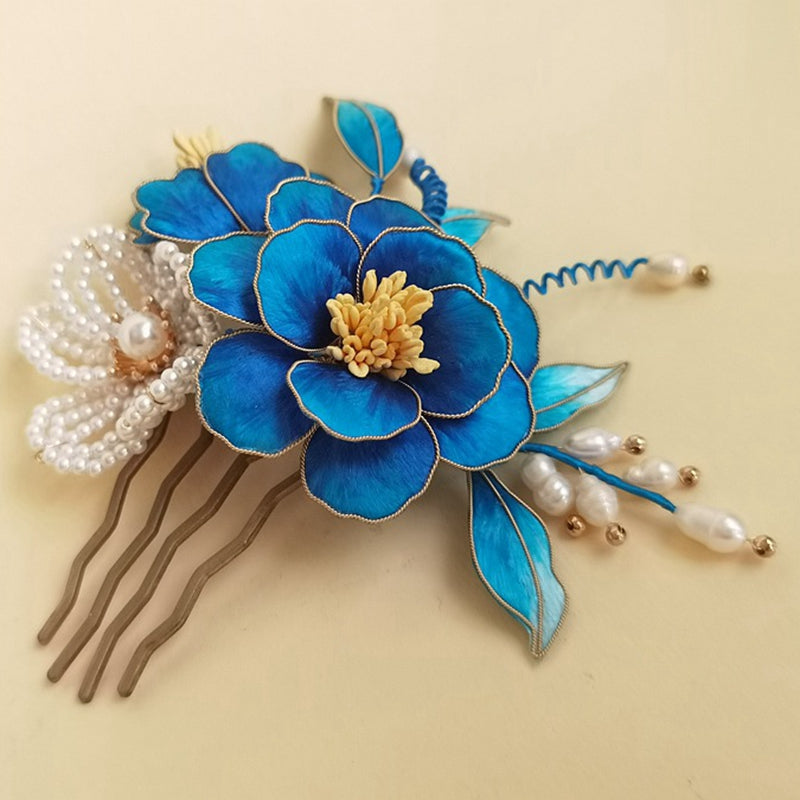 Blue floral ornament perched on a slender stick, shown lying on linen