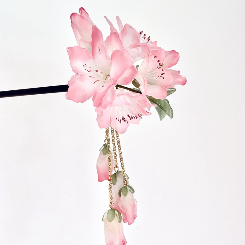 Warm wood-look hair stick with pink azalea-style flowers resting on fabric