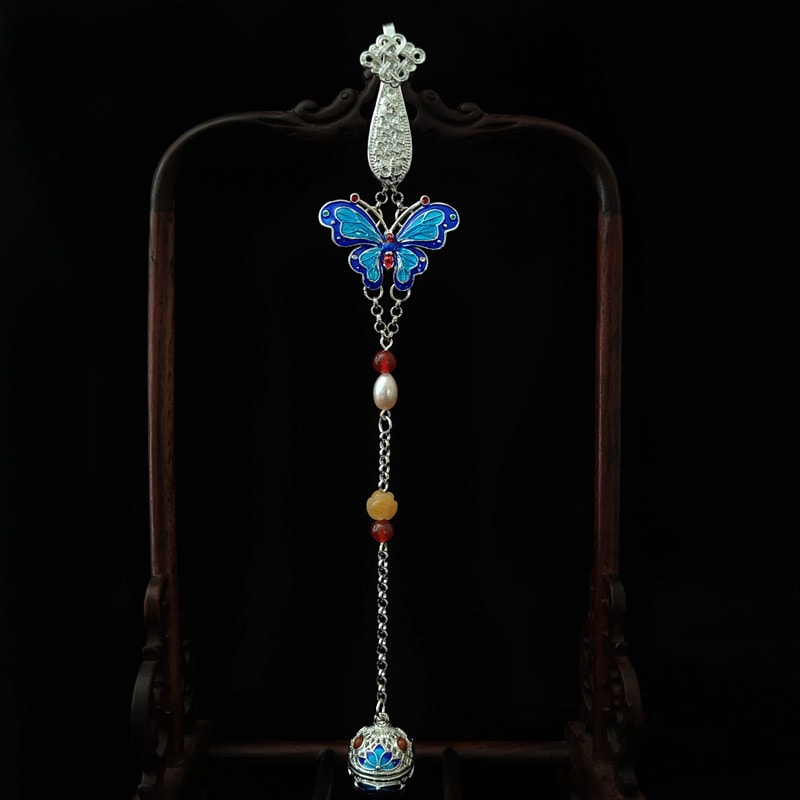 Close-up of butterfly brooch with white tassel and pearl-look beads on fabric