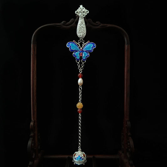 Close-up of butterfly brooch with white tassel and pearl-look beads on fabric