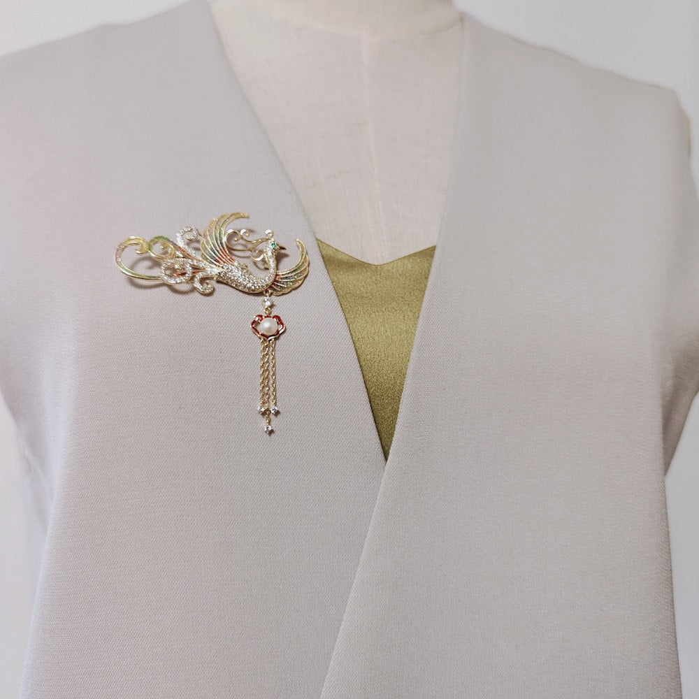 Close-up of enamel-look wings and dangling pearled tassel on silk fabric