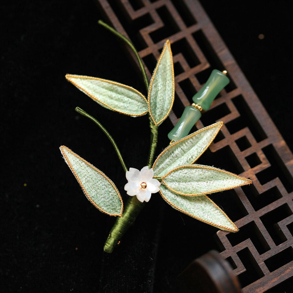 gold-toned bamboo leaf brooch resting on white lattice backdrop, soft light