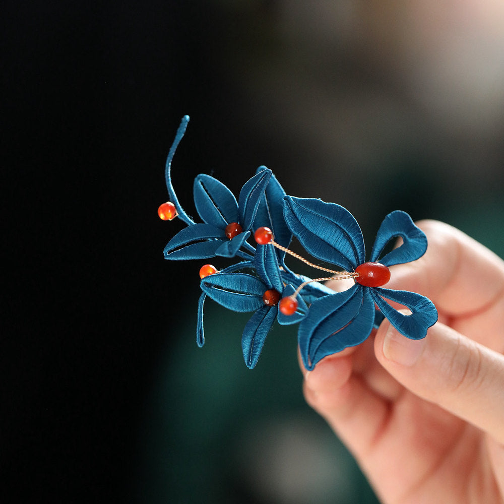 Close-up of the blue flower brooch revealing petal detailing and pearl-like center