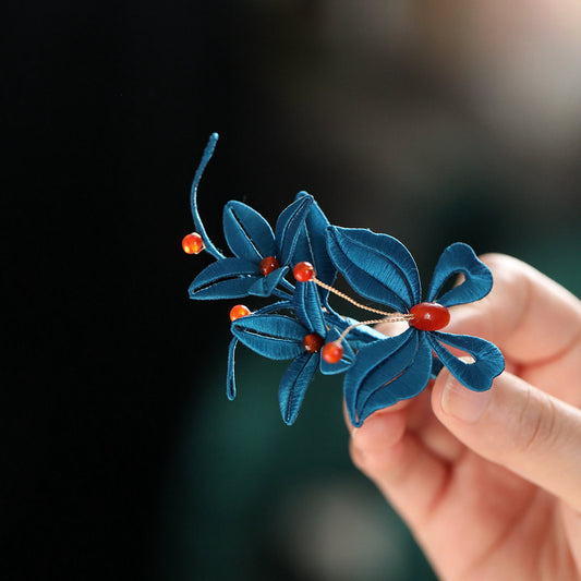 Close-up of the blue flower brooch revealing petal detailing and pearl-like center