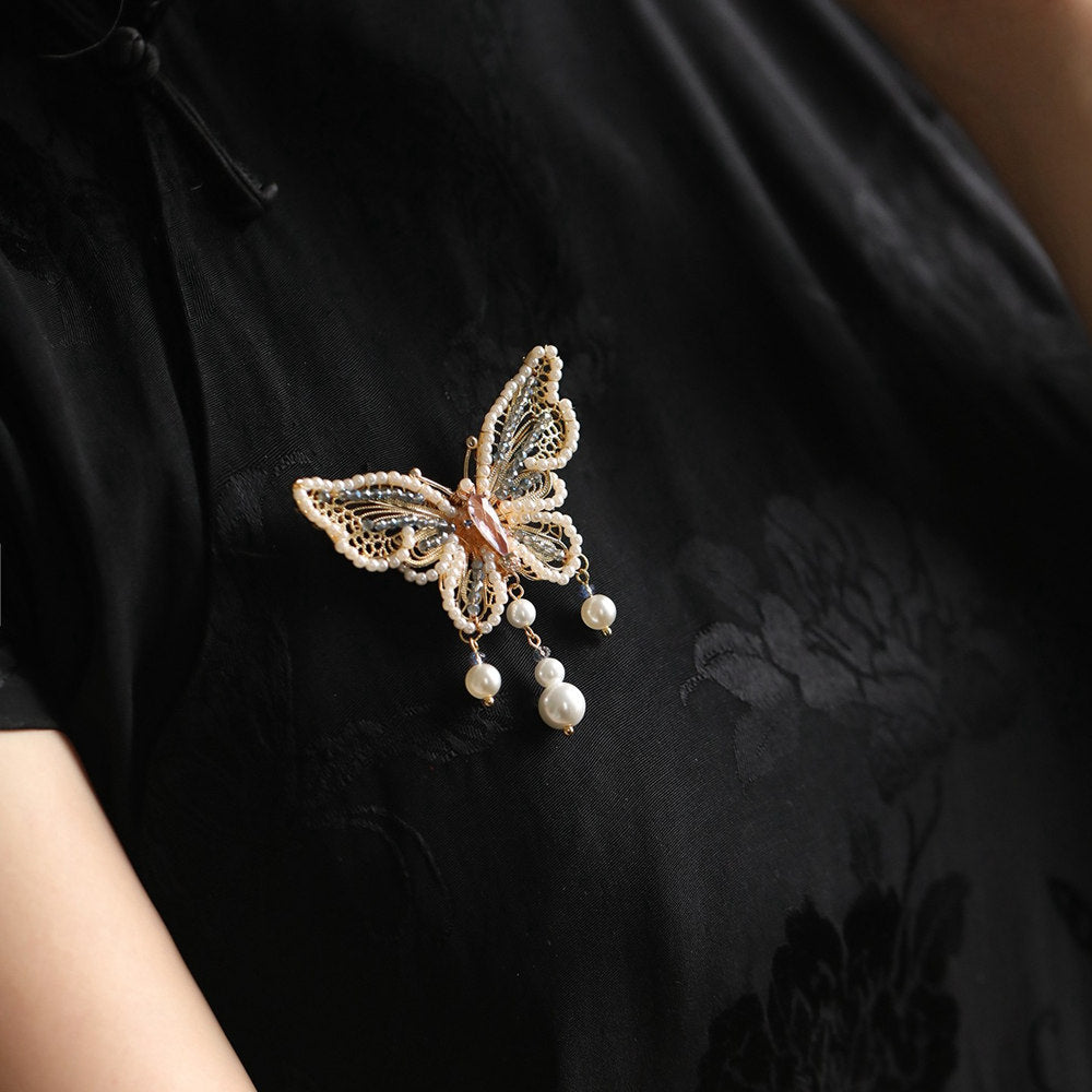 Pearl-accented butterfly brooch pinned on black coat lapel, angled view
