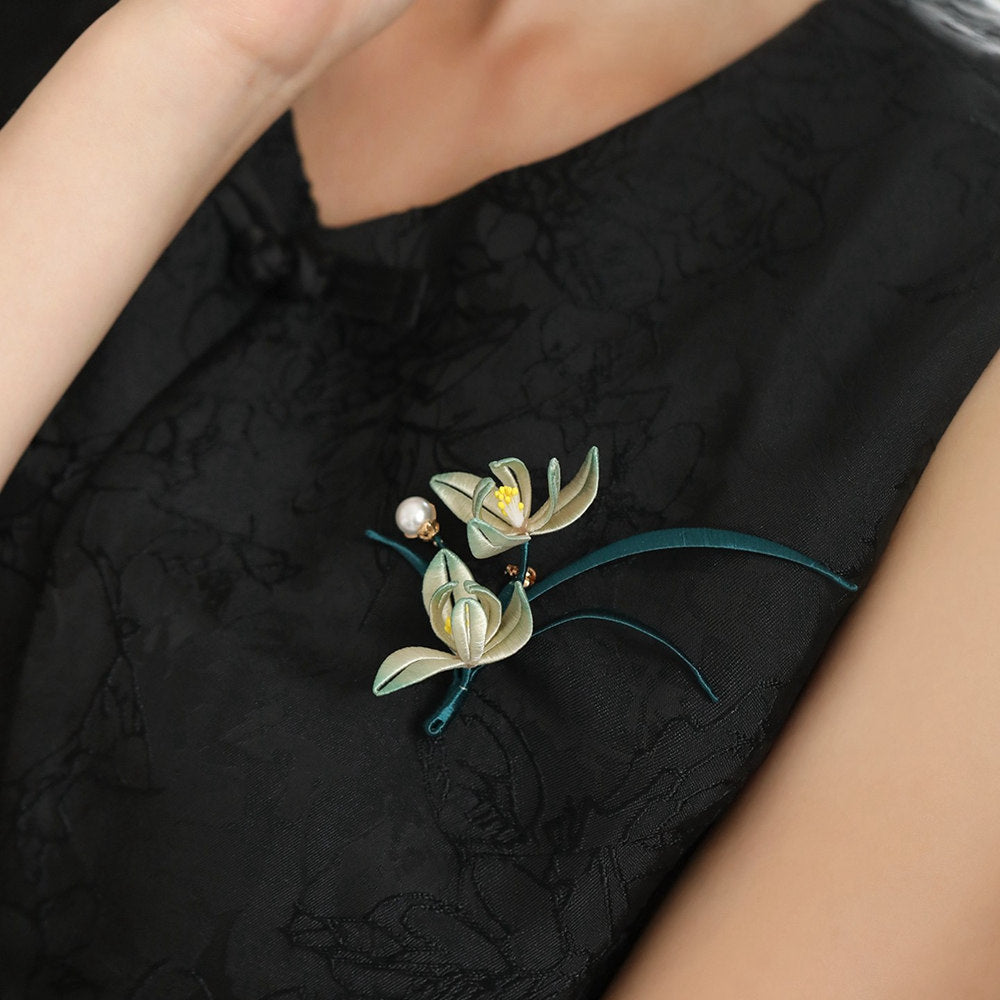 Orchid-shaped floral brooch pinned to black dress, pearl accents and metallic detail