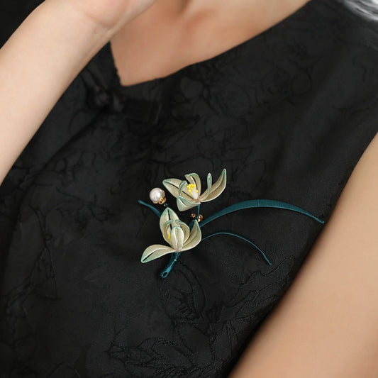 Orchid-shaped floral brooch pinned to black dress, pearl accents and metallic detail