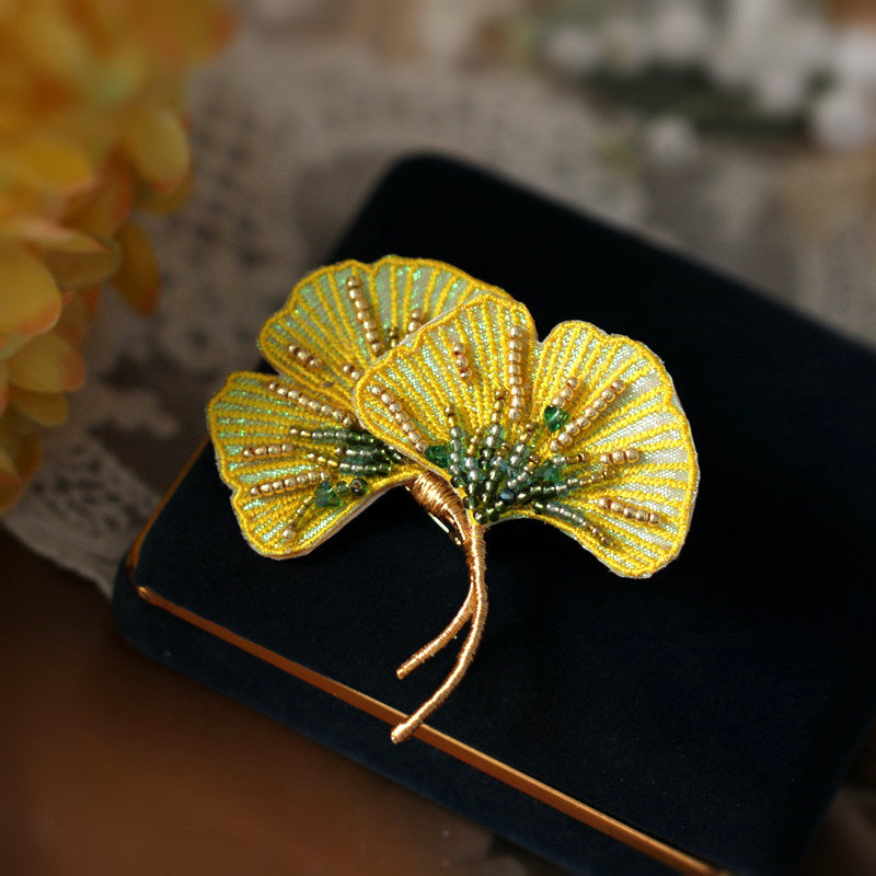 Yellow orchid-inspired brooch lying flat on pale fabric, detailed petal shapes