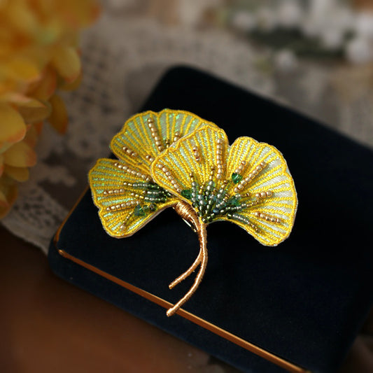 Yellow orchid-inspired brooch lying flat on pale fabric, detailed petal shapes