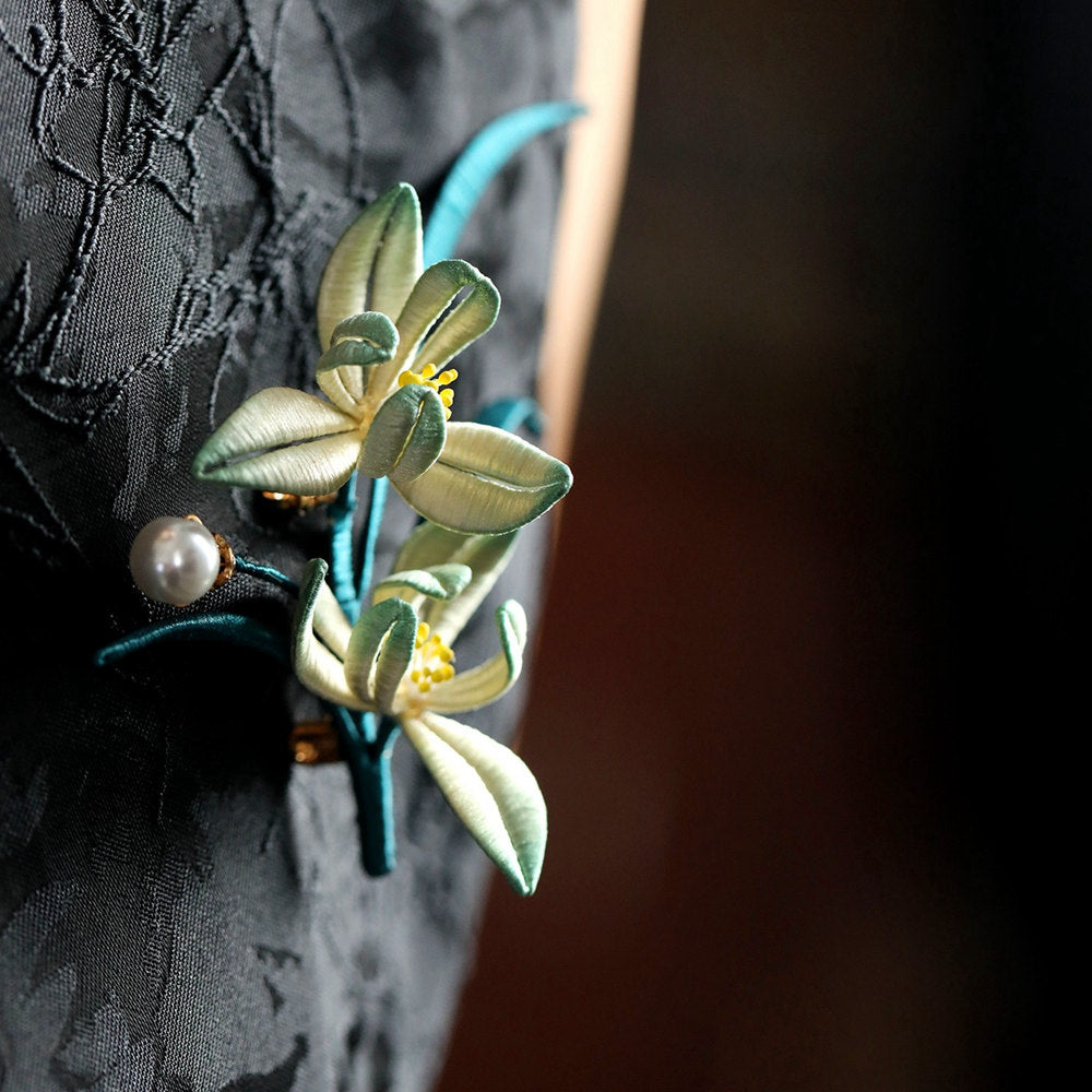 Side view of brooch worn on outerwear, layered petals and gleaming pearl accent