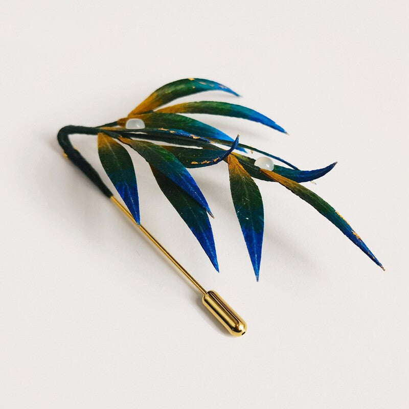 Angled view of green-blue leaf pin on dark wool coat, long stem visible