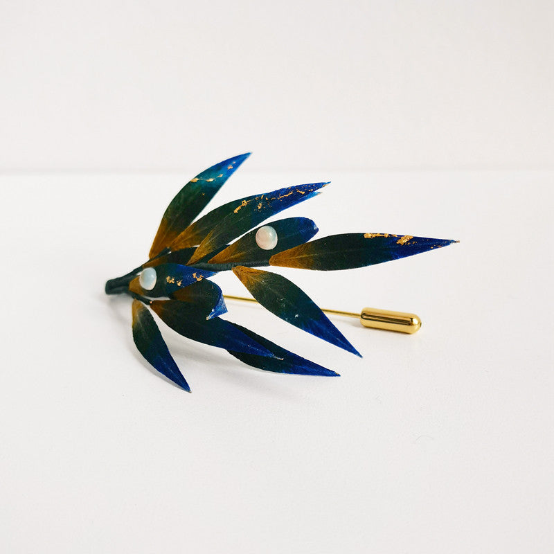Horizontal botanical-style brooch pinned to lapel, overlapping delicate foliage