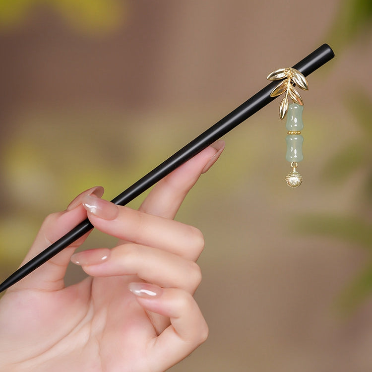 Black wood stick with green jade-like ornament and gold tassel, held in hand
