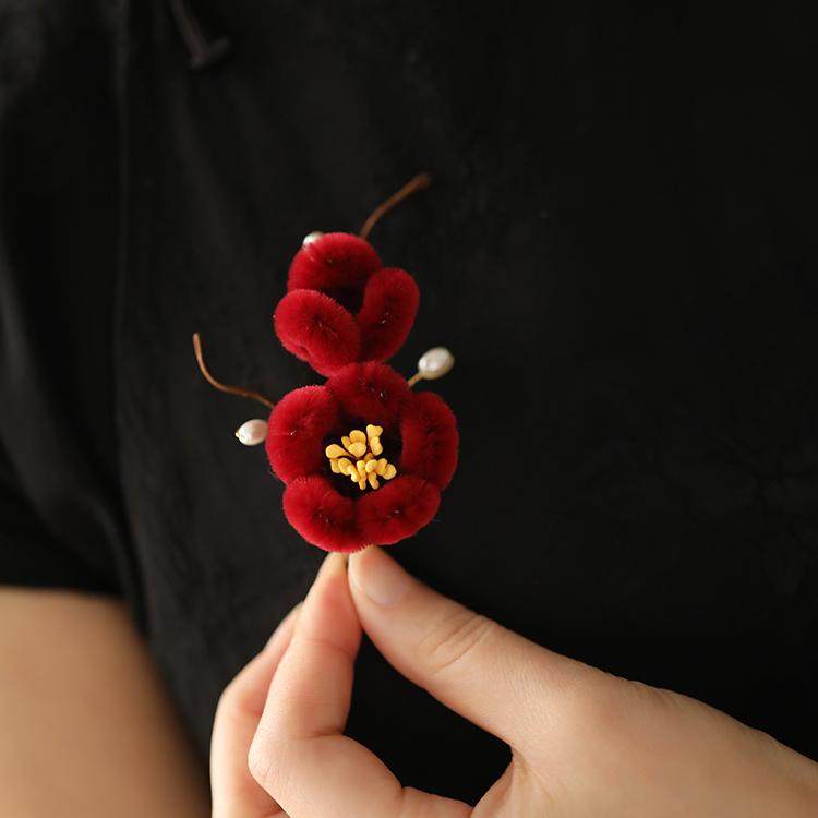 Warm cream plush petal pin held in hand above a wool coat
