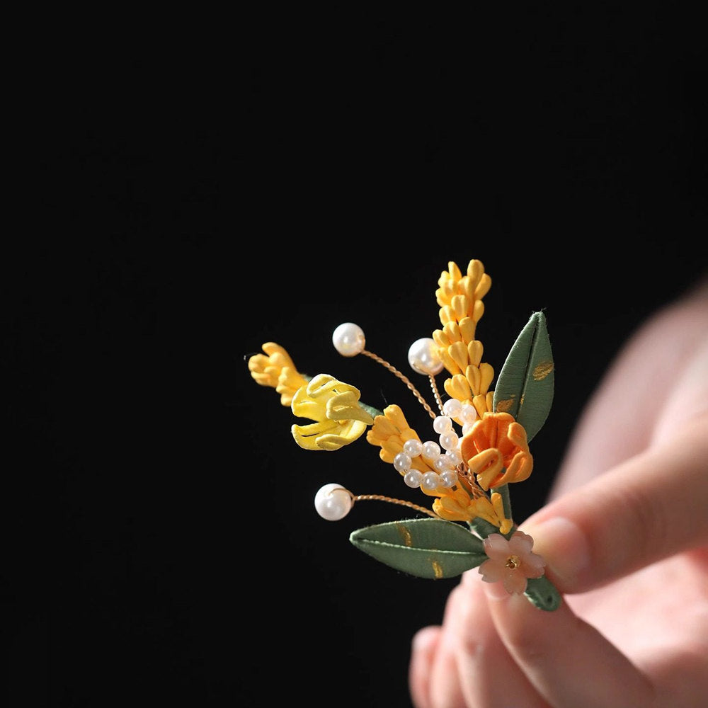 Handheld front view of wheat-inspired floral brooch with pearly accents