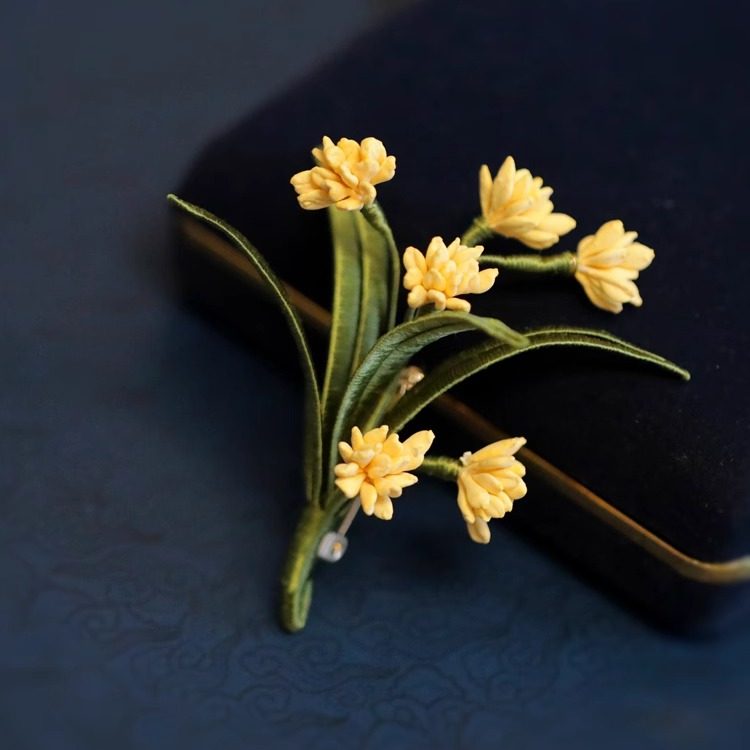 Top view of golden osmanthus-inspired floral pin with pale pearl accents on neutral background