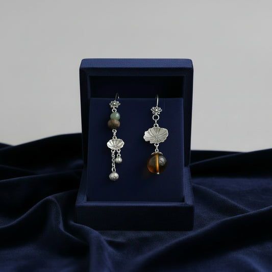 Hand holding two silver floral earrings with beads against a blurred background