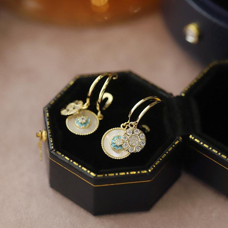 Gold earrings with gemstones in a black jewelry box on a beige surface