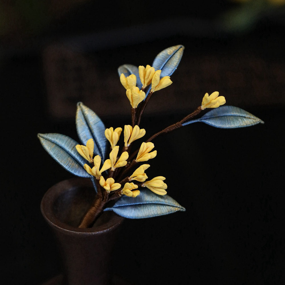Artistic display of layered blossom pin on black fabric, warm metallic finish
