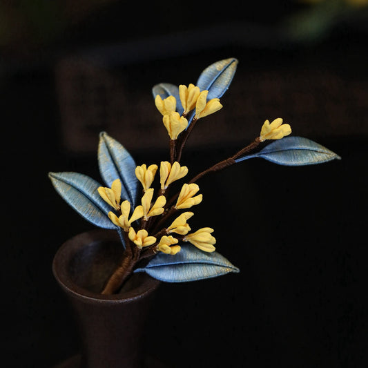 Artistic display of layered blossom pin on black fabric, warm metallic finish