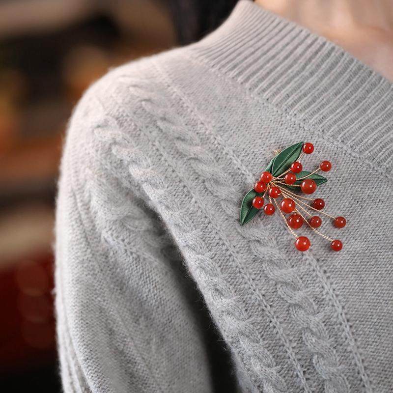 Red berry brooch pinned to cream sweater near the shoulder, angled view