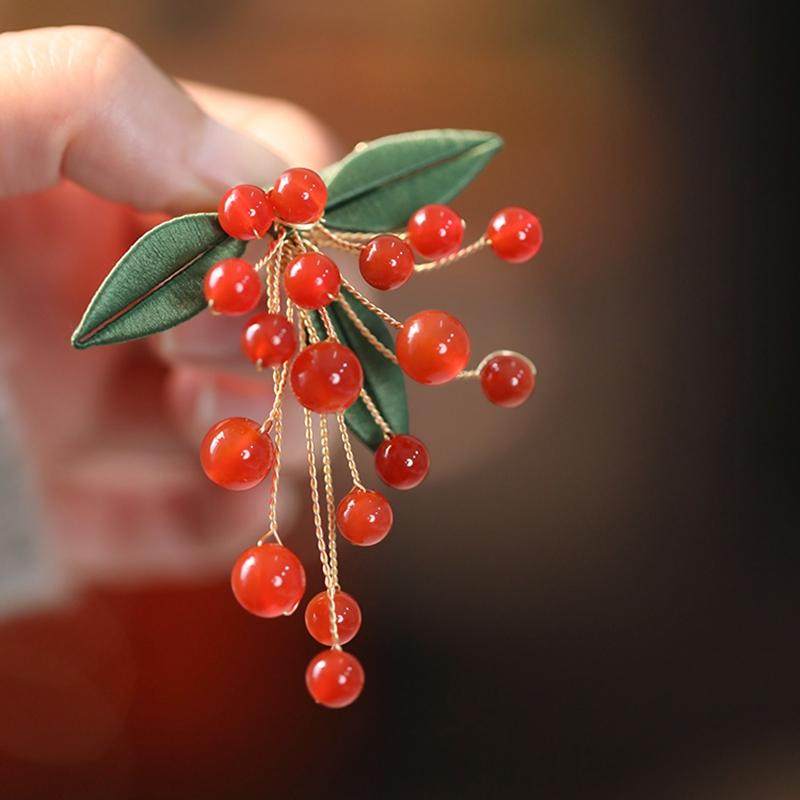 Side angle showing glossy red berries and gold-toned pin fastening detail